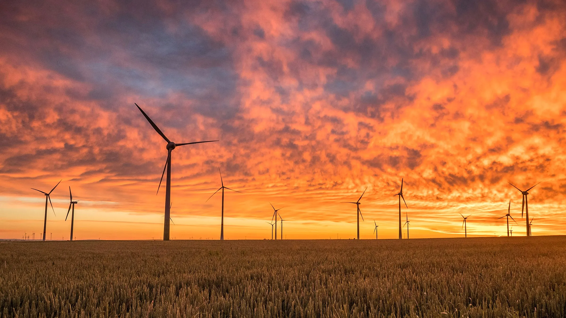 Wind turbines silhouetted against a fiery orange sunset